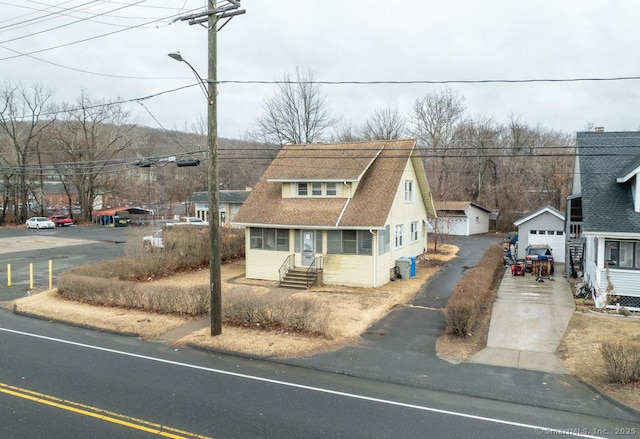 view of front of property with entry steps, a shingled roof, an outdoor structure, a detached garage, and driveway