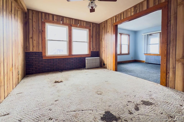 empty room with radiator, wood walls, ceiling fan, and carpet flooring