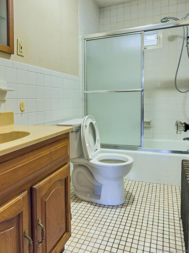 bathroom with tile walls, toilet, enclosed tub / shower combo, vanity, and tile patterned flooring