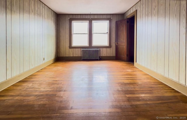 unfurnished room featuring radiator heating unit, baseboards, and wood finished floors