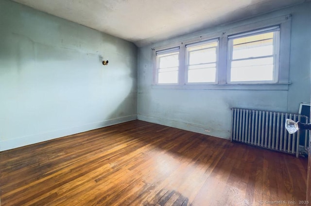 unfurnished room with radiator heating unit, baseboards, and wood-type flooring