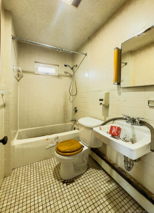 bathroom featuring a textured ceiling, toilet, shower / bath combination, a sink, and tile walls