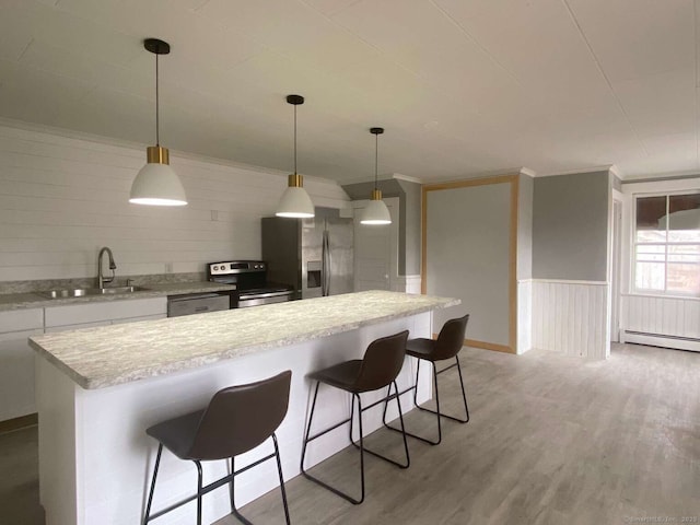 kitchen featuring light wood finished floors, light countertops, appliances with stainless steel finishes, wainscoting, and a sink