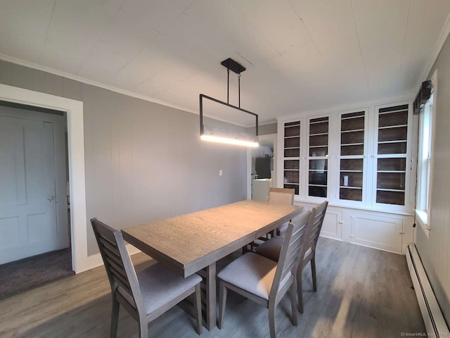 dining area featuring crown molding, a baseboard heating unit, a decorative wall, and wood finished floors