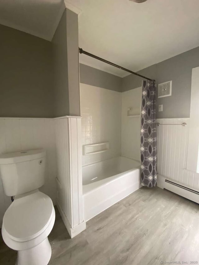 full bathroom with toilet, a wainscoted wall, wood finished floors, visible vents, and shower / bath combo with shower curtain