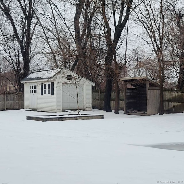 snow covered structure with fence and an outdoor structure