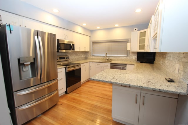 kitchen with stainless steel appliances, a peninsula, a sink, light wood-style floors, and decorative backsplash