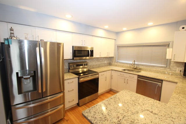 kitchen featuring appliances with stainless steel finishes, a sink, light stone counters, and white cabinetry