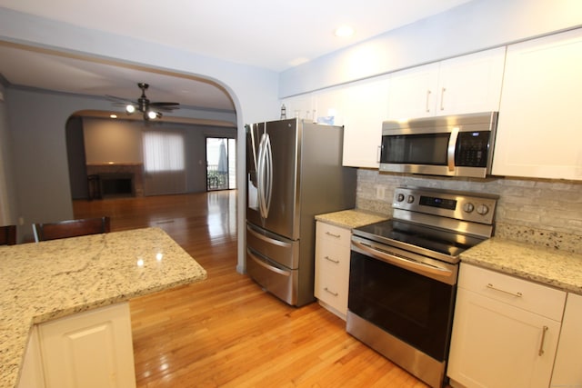 kitchen with light wood finished floors, arched walkways, decorative backsplash, a ceiling fan, and stainless steel appliances