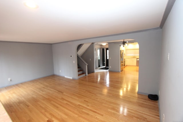 empty room featuring arched walkways, ceiling fan, light wood-style floors, stairway, and crown molding