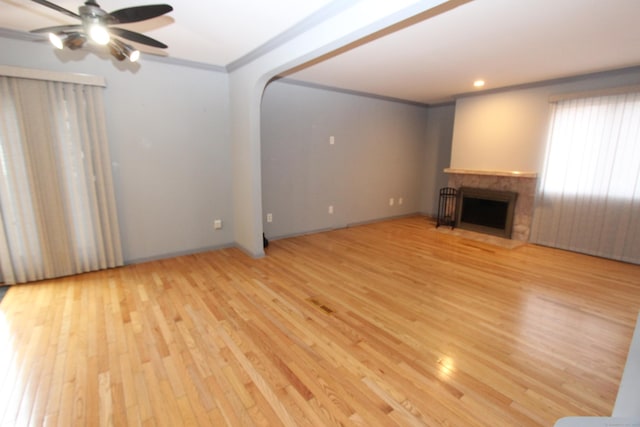 unfurnished living room with arched walkways, light wood finished floors, a fireplace with flush hearth, ornamental molding, and ceiling fan