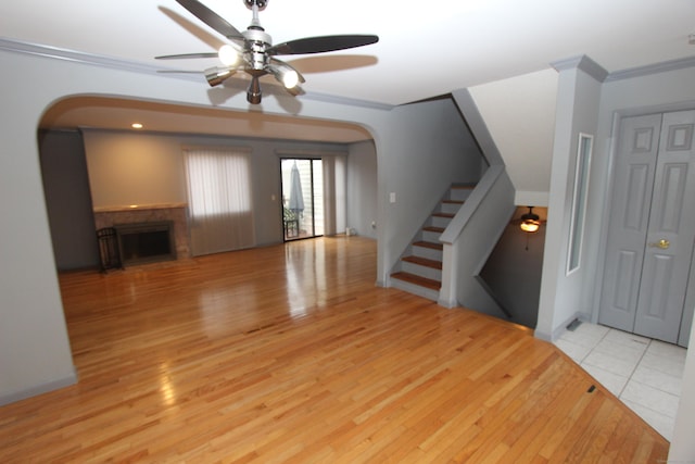 unfurnished living room with arched walkways, a fireplace, stairway, light wood-style flooring, and ornamental molding