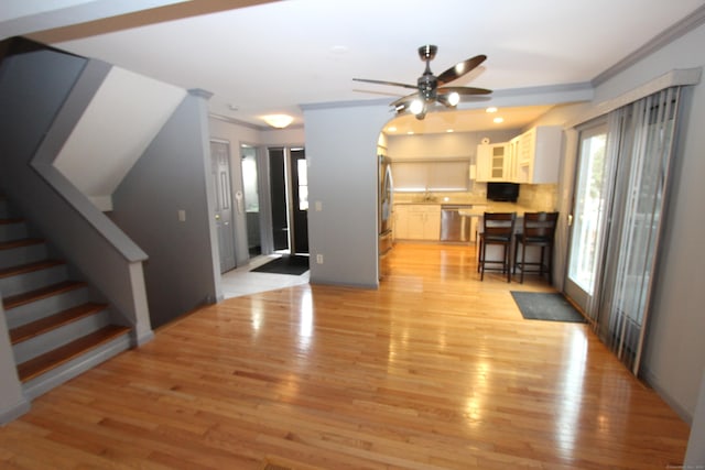 unfurnished living room featuring ornamental molding, stairway, a ceiling fan, and light wood-style floors