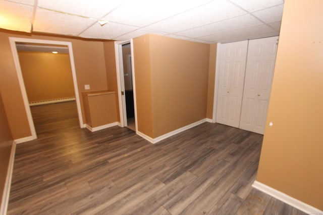 unfurnished room featuring dark wood-type flooring, a baseboard radiator, a drop ceiling, and baseboards