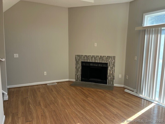 unfurnished living room with a fireplace with raised hearth, baseboards, and wood finished floors