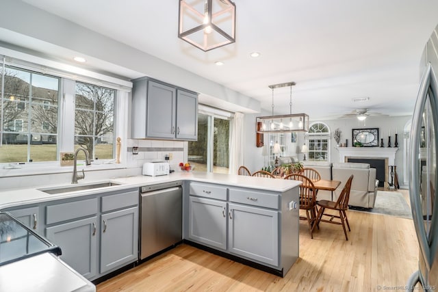 kitchen with a peninsula, a fireplace, a sink, appliances with stainless steel finishes, and gray cabinets