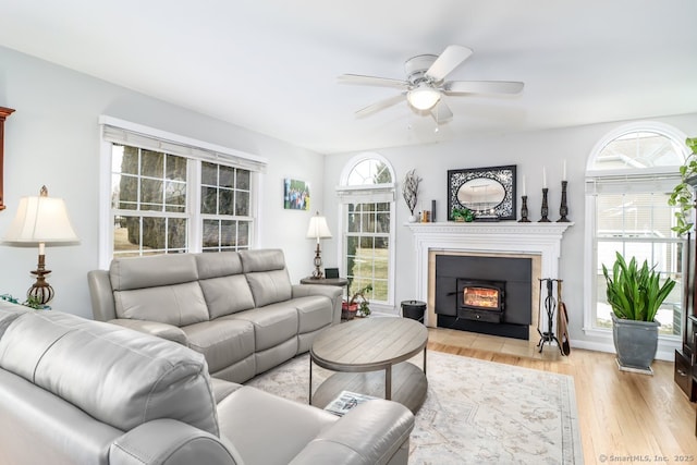 living room with ceiling fan, a fireplace with flush hearth, and light wood-style flooring