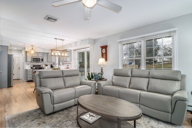 living area featuring ceiling fan with notable chandelier, light wood-type flooring, and visible vents