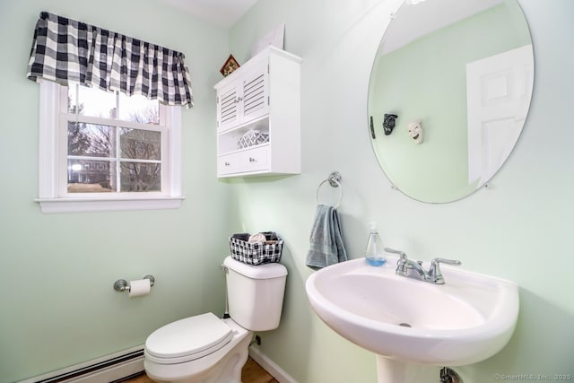 half bath featuring a baseboard heating unit, baseboards, a sink, and toilet