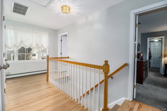 hall featuring baseboards, visible vents, wood finished floors, an upstairs landing, and a baseboard heating unit