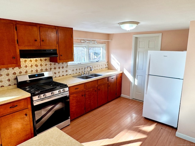 kitchen featuring under cabinet range hood, a sink, light countertops, freestanding refrigerator, and gas range