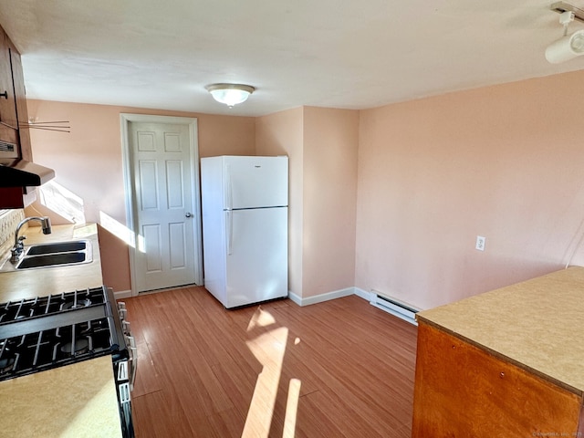 kitchen with a baseboard radiator, a sink, freestanding refrigerator, light wood finished floors, and range with gas cooktop