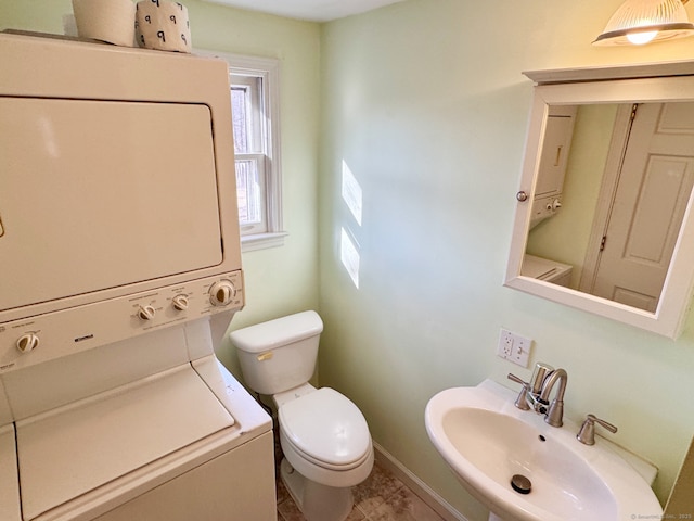 bathroom with a sink, baseboards, toilet, and stacked washer / drying machine