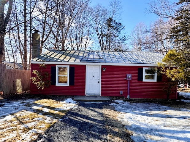 view of front of house with a standing seam roof, fence, a chimney, and metal roof