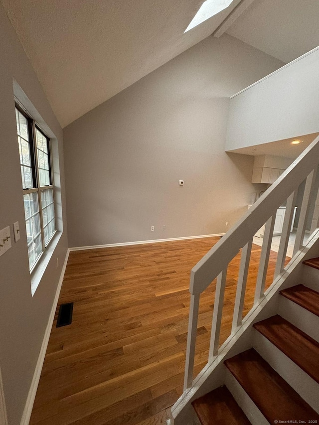 staircase with a textured ceiling, vaulted ceiling with skylight, wood finished floors, visible vents, and baseboards