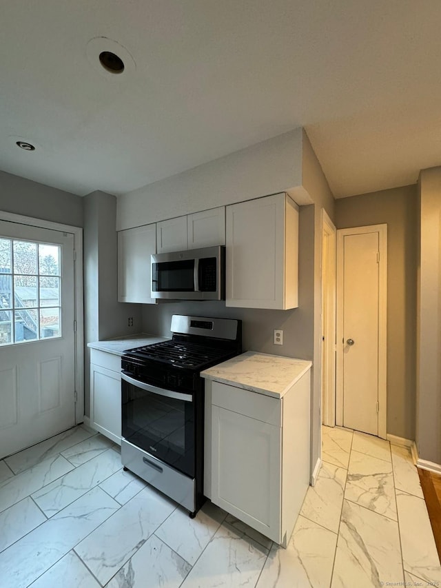 kitchen featuring marble finish floor, light countertops, appliances with stainless steel finishes, white cabinetry, and baseboards