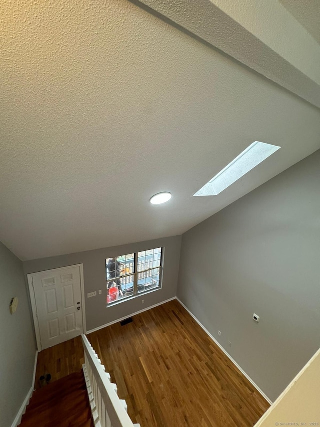 foyer entrance featuring vaulted ceiling with skylight, visible vents, baseboards, dark wood finished floors, and a textured ceiling