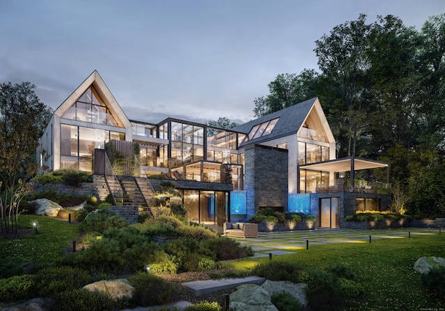 back of property with a yard, stone siding, a balcony, and stairs