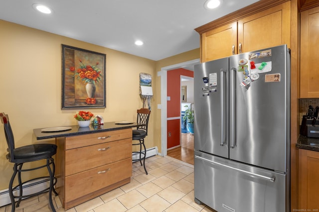 kitchen with a baseboard heating unit, high quality fridge, brown cabinetry, and a kitchen bar