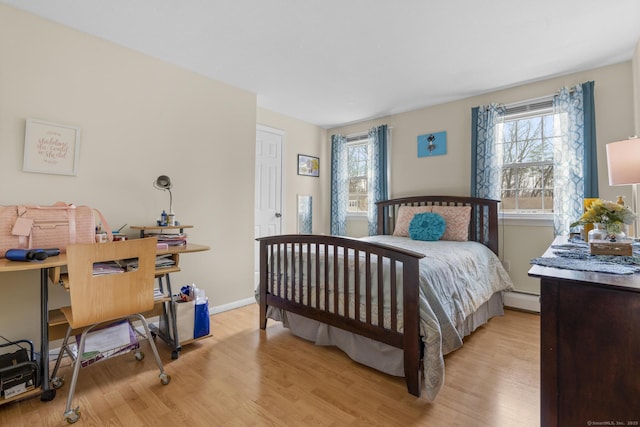 bedroom with a baseboard heating unit, light wood-style flooring, and baseboards