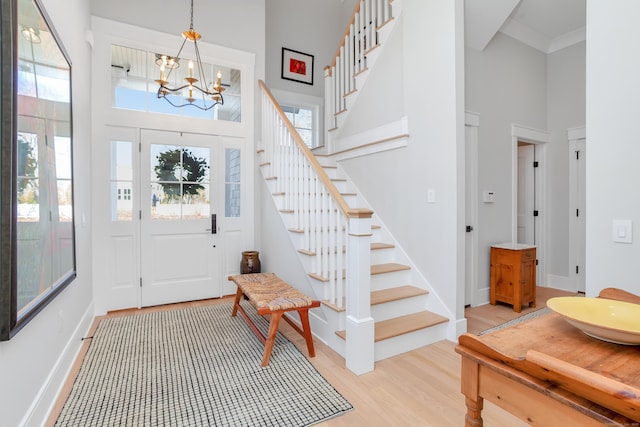 foyer entrance featuring a chandelier, a towering ceiling, baseboards, stairs, and light wood-style floors