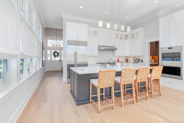 kitchen with tasteful backsplash, appliances with stainless steel finishes, ornamental molding, light countertops, and under cabinet range hood