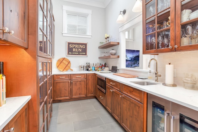 kitchen featuring a sink, brown cabinets, tasteful backsplash, stainless steel microwave, and glass insert cabinets