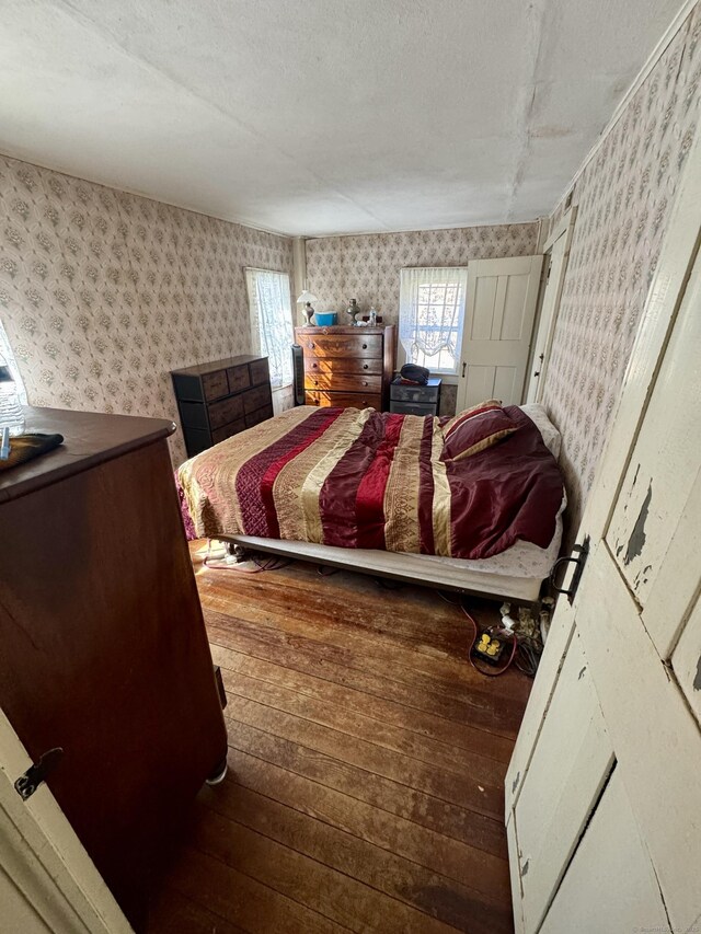 bedroom featuring a textured ceiling, hardwood / wood-style flooring, and wallpapered walls