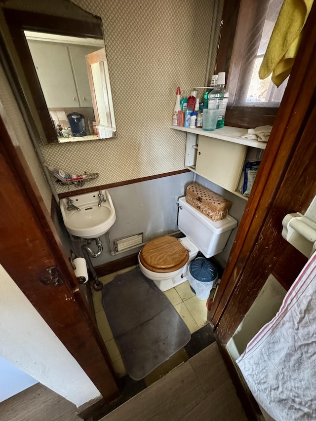 half bathroom with tile patterned flooring, a sink, toilet, and wallpapered walls