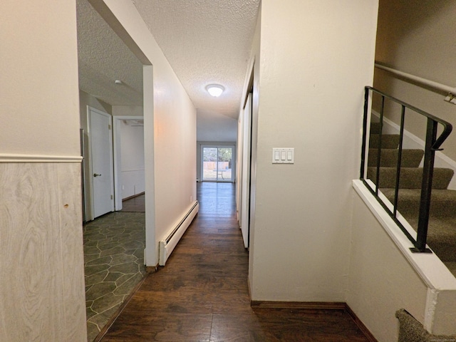 hall with dark wood finished floors, stairway, a baseboard heating unit, a textured ceiling, and baseboards