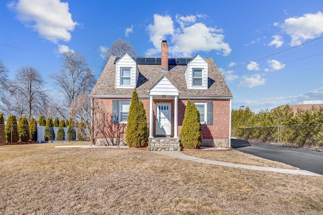 new england style home featuring solar panels, brick siding, and fence