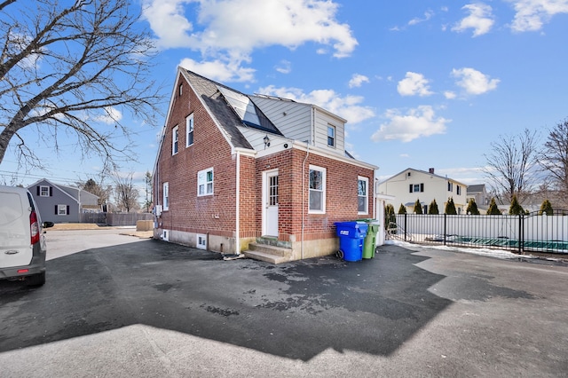 view of side of property featuring entry steps, brick siding, fence, and a residential view