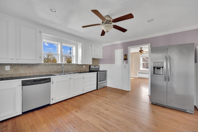 kitchen with stainless steel appliances, radiator heating unit, a sink, and white cabinetry