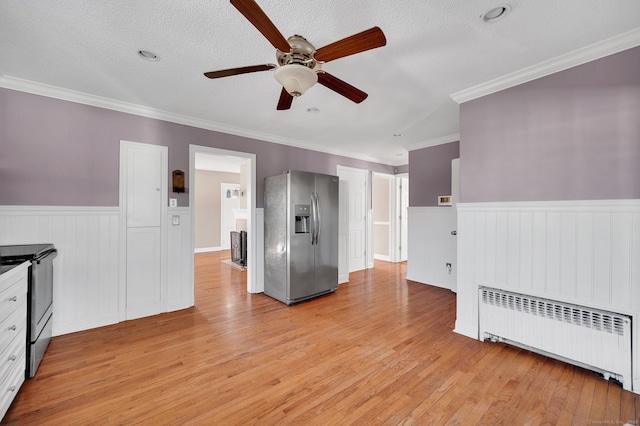 kitchen featuring light wood-type flooring, radiator heating unit, stainless steel appliances, and wainscoting