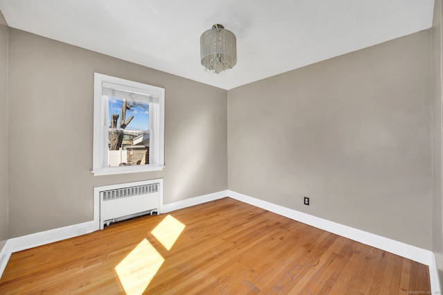 unfurnished room with a chandelier, baseboards, radiator heating unit, and wood finished floors