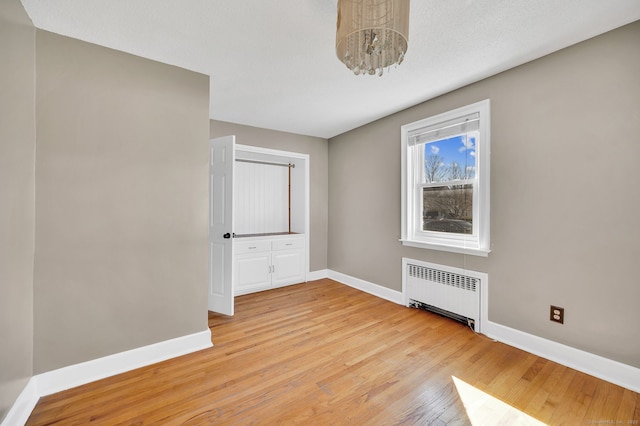 unfurnished bedroom featuring light wood-style floors, baseboards, and radiator heating unit