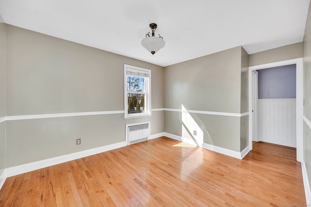 spare room featuring radiator, light wood-style floors, baseboards, and wainscoting