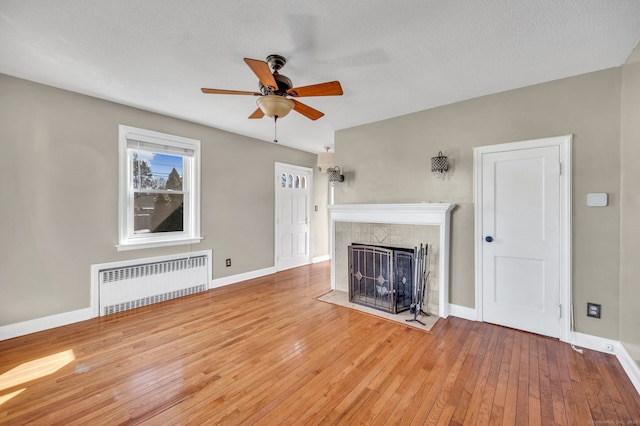 unfurnished living room with ceiling fan, baseboards, hardwood / wood-style floors, radiator heating unit, and a tiled fireplace