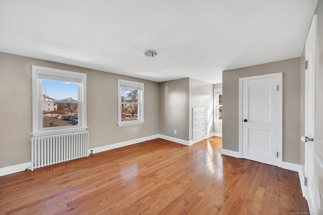 empty room with baseboards, light wood-style flooring, and radiator heating unit