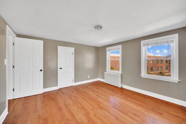 unfurnished bedroom featuring light wood-type flooring, radiator, and baseboards